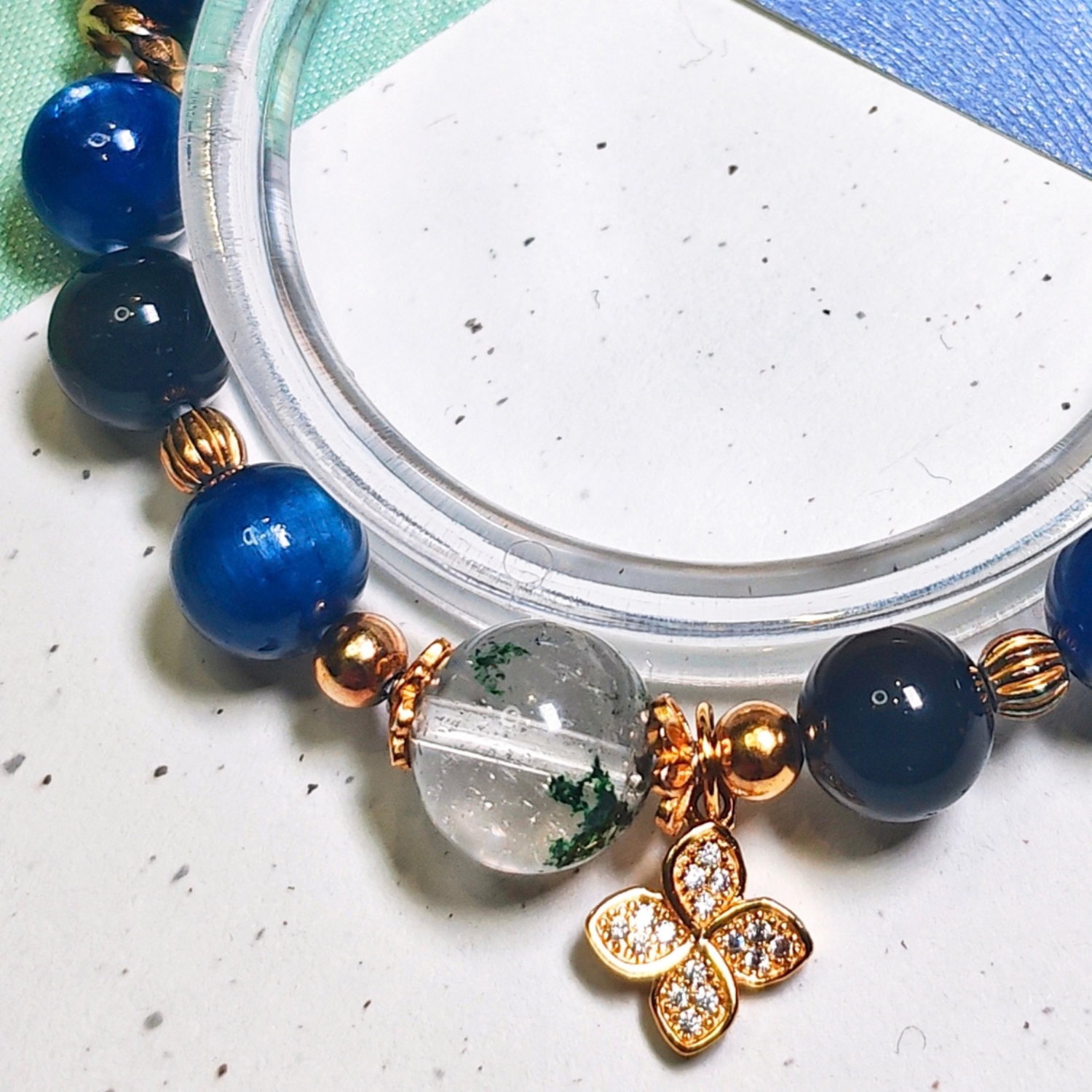 Close view of the green phantom quartz bracelet, showing its deep blue kyanite beads and four-leaf clover charm.