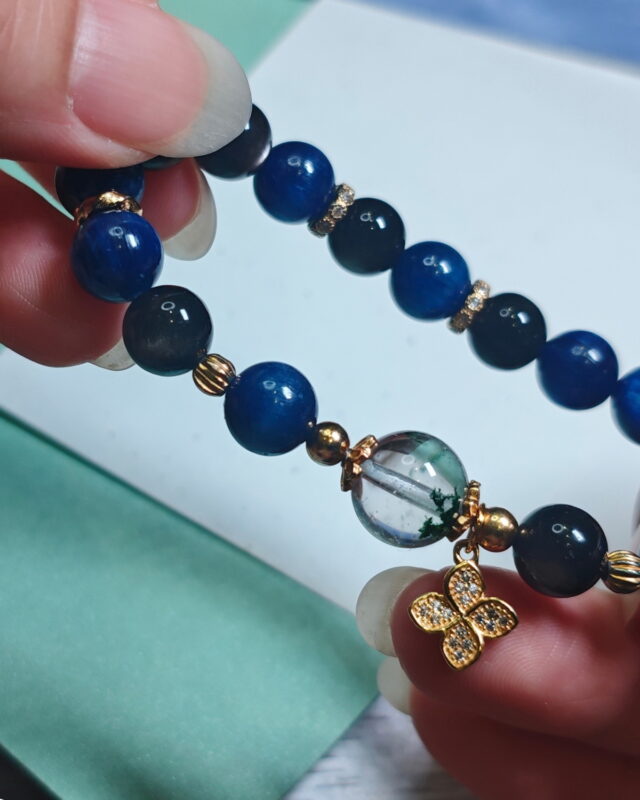 Green phantom quartz bracelet held in hand, showing the deep blue kyanite, green phantom quartz and silver obsidian beads.