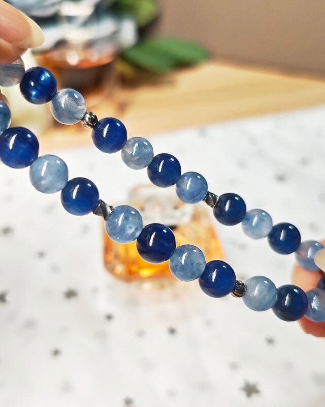 Still blue crystal bracelet held open between both hands, deep and pale blue kyanite beads with silver spacers