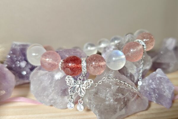 Strawberry quartz crystal bracelet with pink speckled beads and silver butterfly charm on quartz cluster