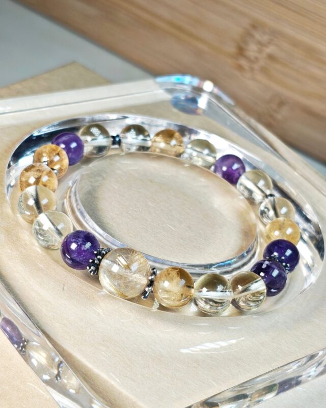 Sunlit hush crystal bracelet resting on a clear acrylic stand beside a wooden tray