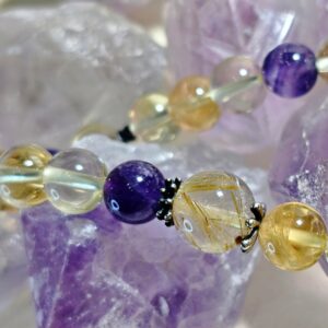 Close view of golden rutilated quartz and amethyst beads against a cluster of amethyst points