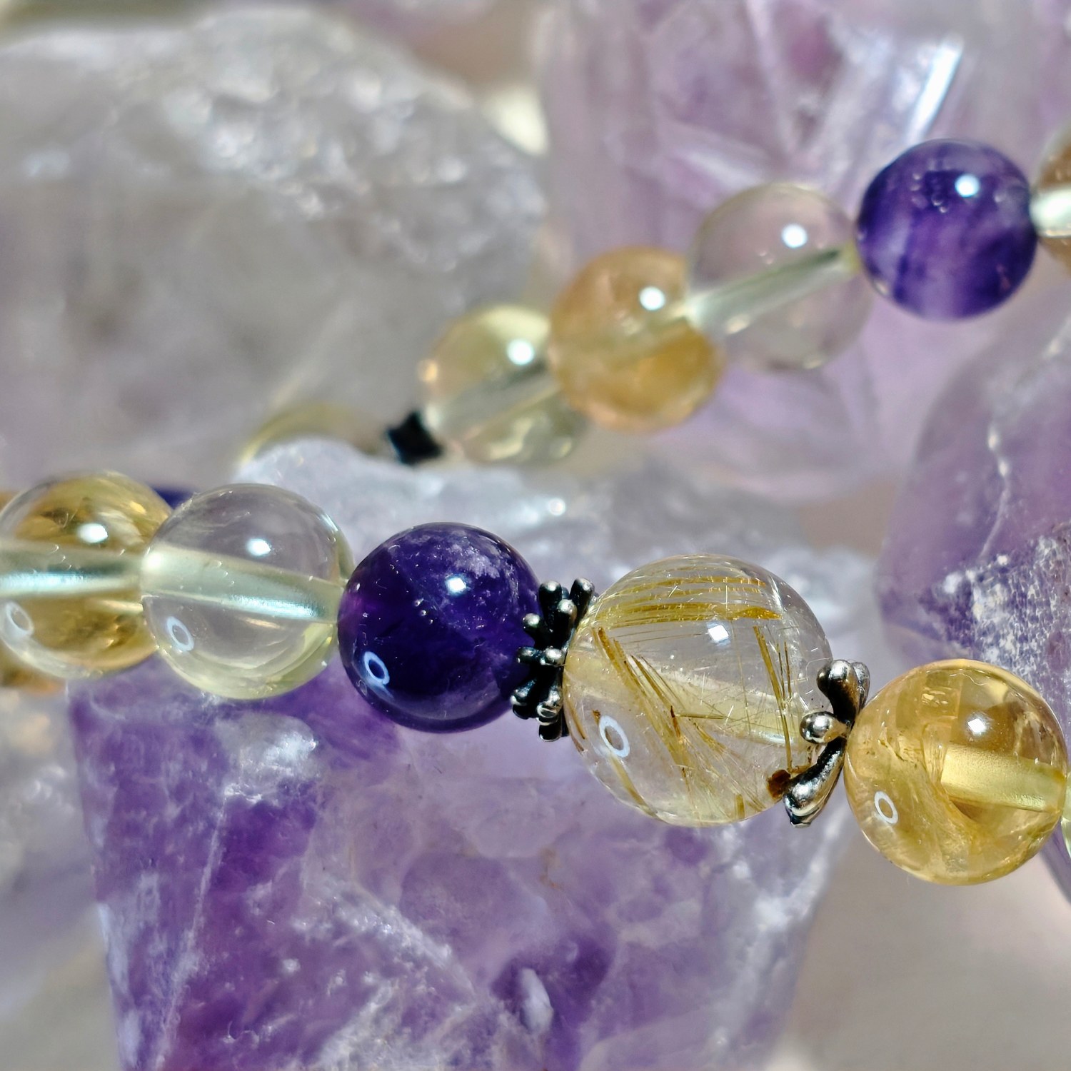 Close view of golden rutilated quartz and amethyst beads against a cluster of amethyst points