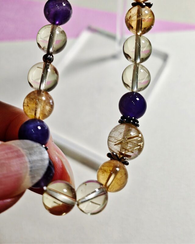Bracelet held between two fingers, golden rutilated quartz and amethyst beads with s925 sterling silver spacers