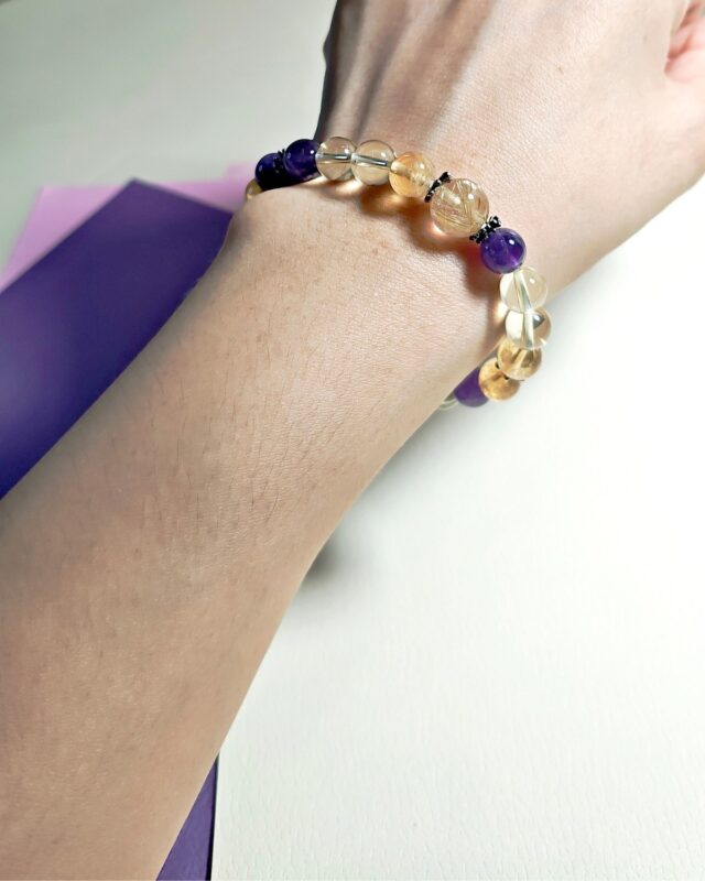 Golden rutilated quartz citrine and amethyst bracelet worn on the wrist in daylight