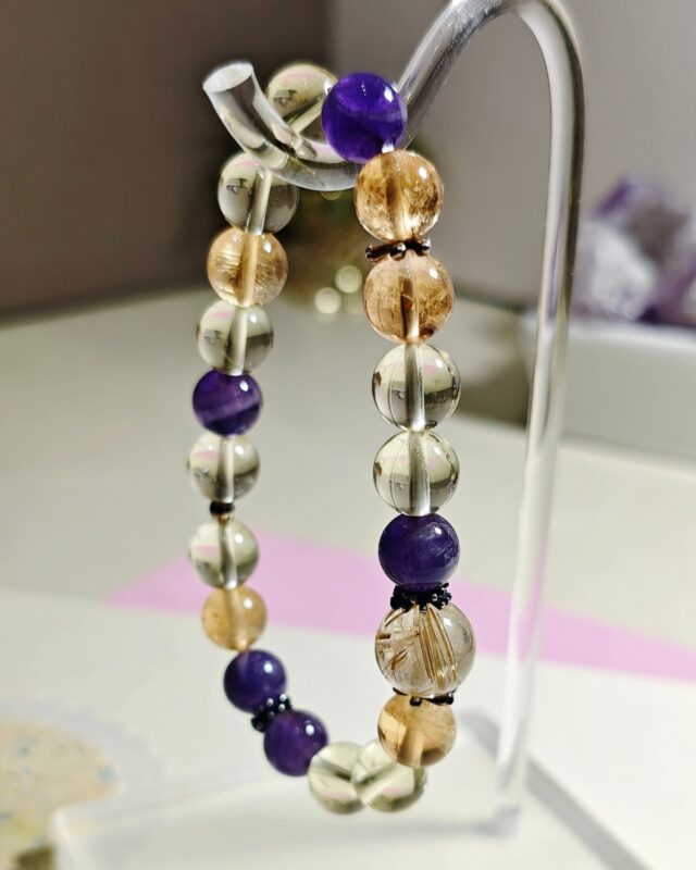 Golden rutilated quartz citrine and amethyst bracelet draped over a clear acrylic stand