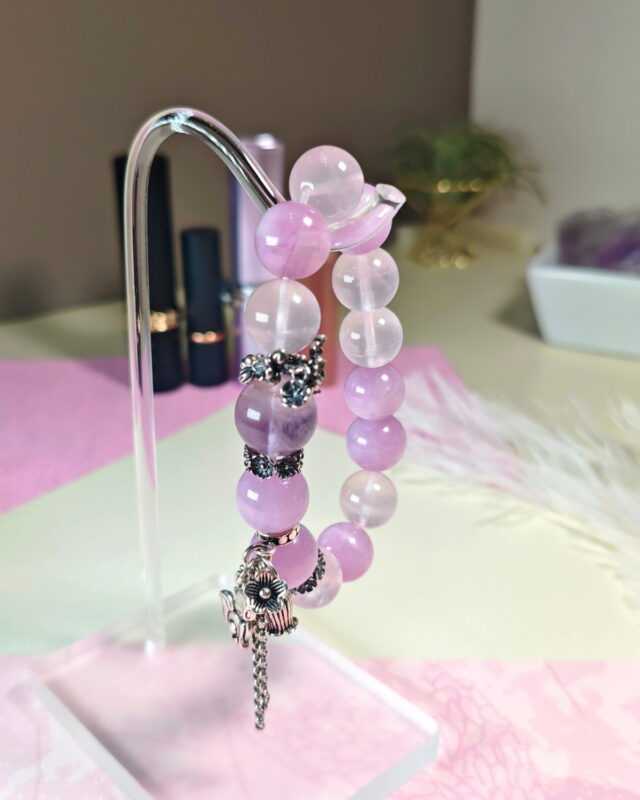 Tender Charm crystal bracelet hung on a clear stand over pale pink cloth.