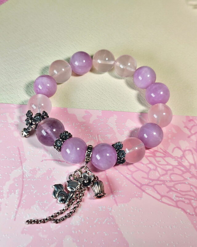Purple rutilated quartz bracelet on soft pink floral paper, with its sterling silver nine-tailed fox charm at the front.